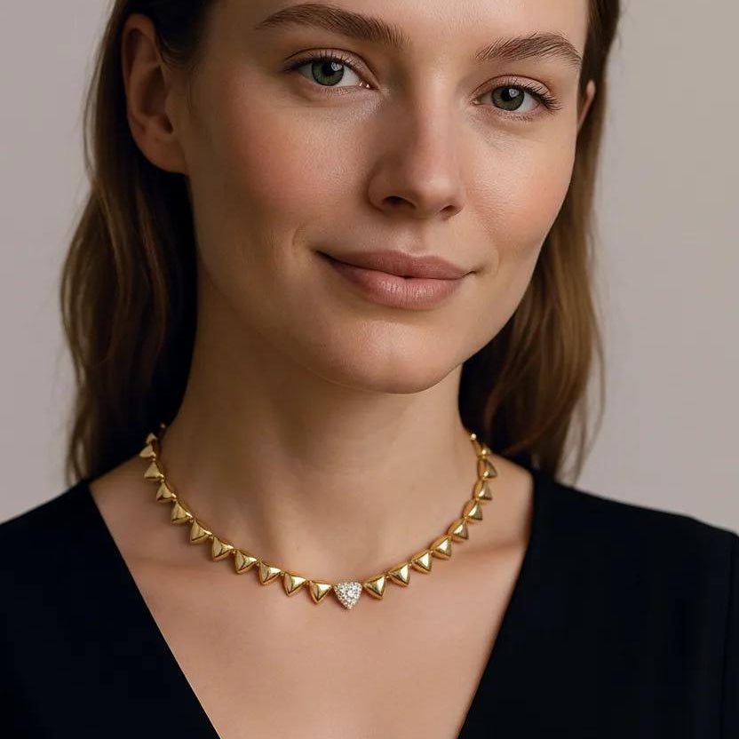 Woman wearing a gold necklace with a clear gemstone against a neutral background