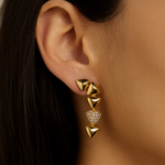 Gold pyramid-shaped earrings worn by a person with dark hair.