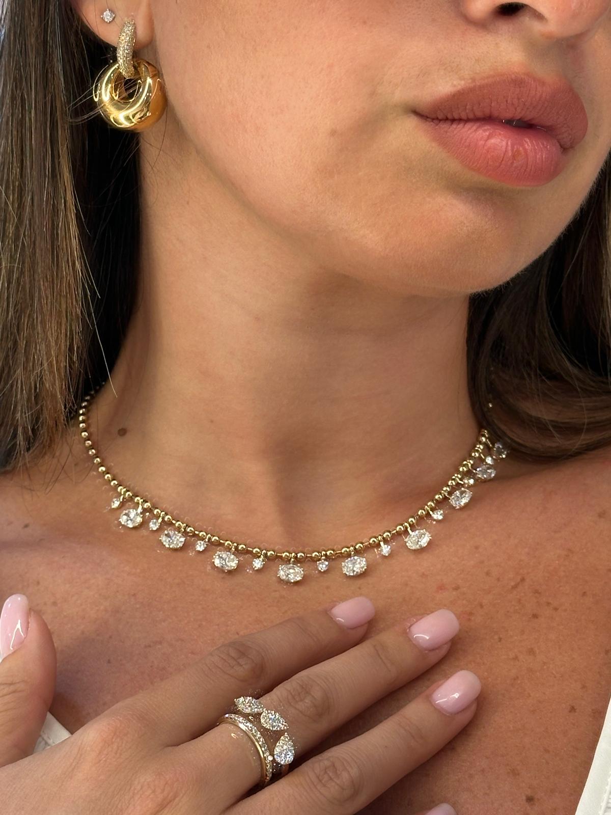 Close-up of a woman wearing a gold necklace and gold hoop earrings with a ring on her finger.