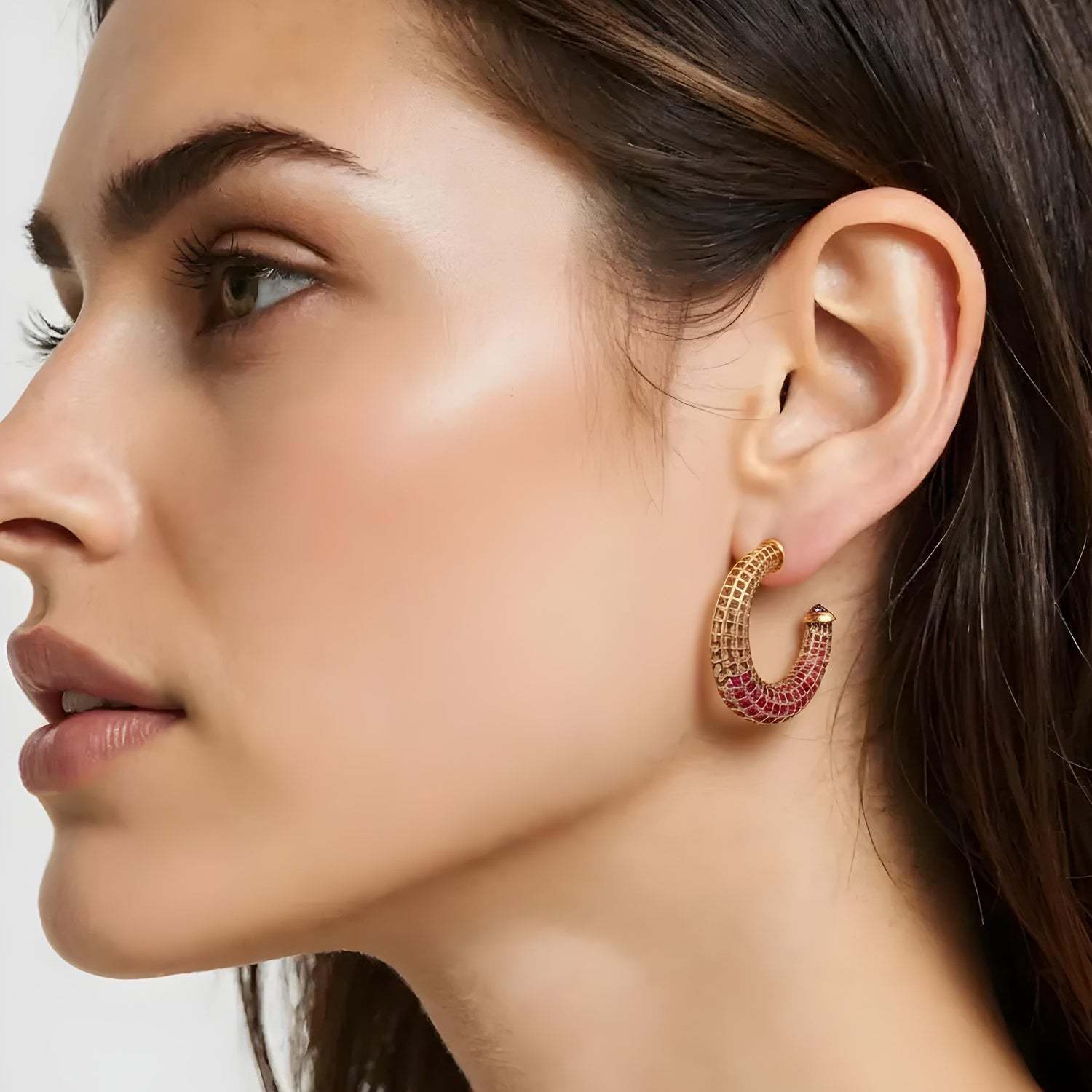 Close-up of a woman wearing a gold and red earring on a white background